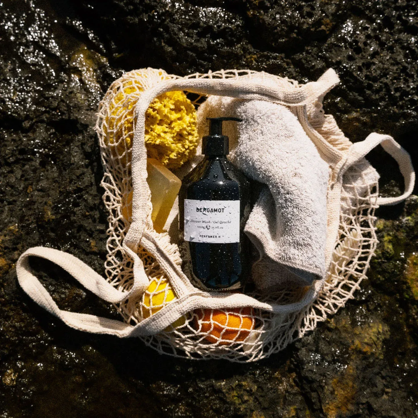 Perfumer H 沐浴瓶放在網袋裡,與柑橘一起置於海岸岩石